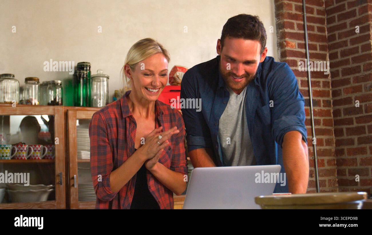 Young Couple Using Laptop In Open Plan Apartment Kitchen Stock Photo