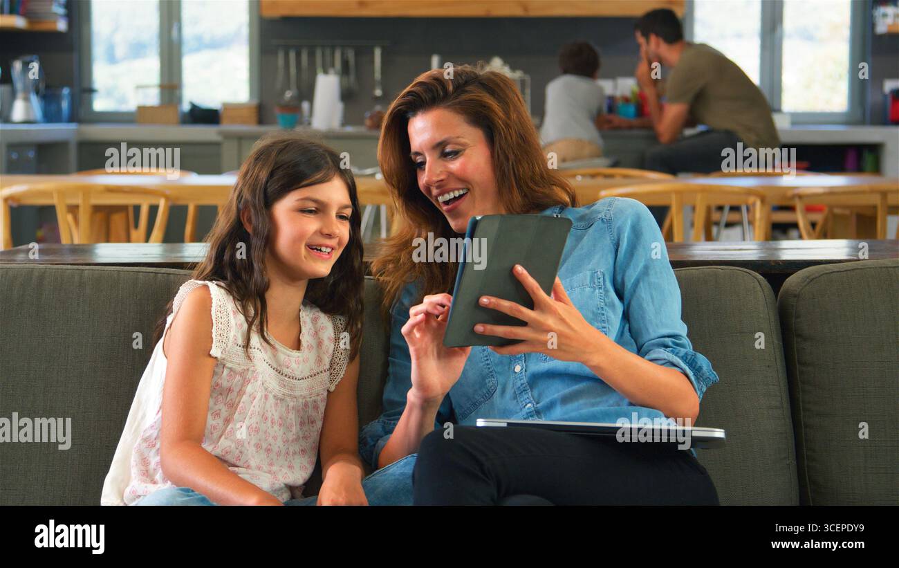 Mother And Daughter Sitting On Lounge Sofa Using Digital Tablet And Laptop Stock Photo
