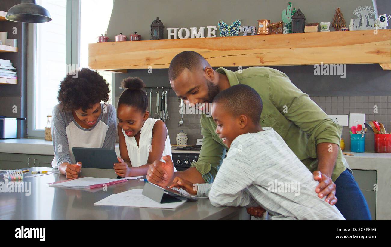 Parents Helping Children With Homework Using Digital Tablets In Kitchen Stock Photo