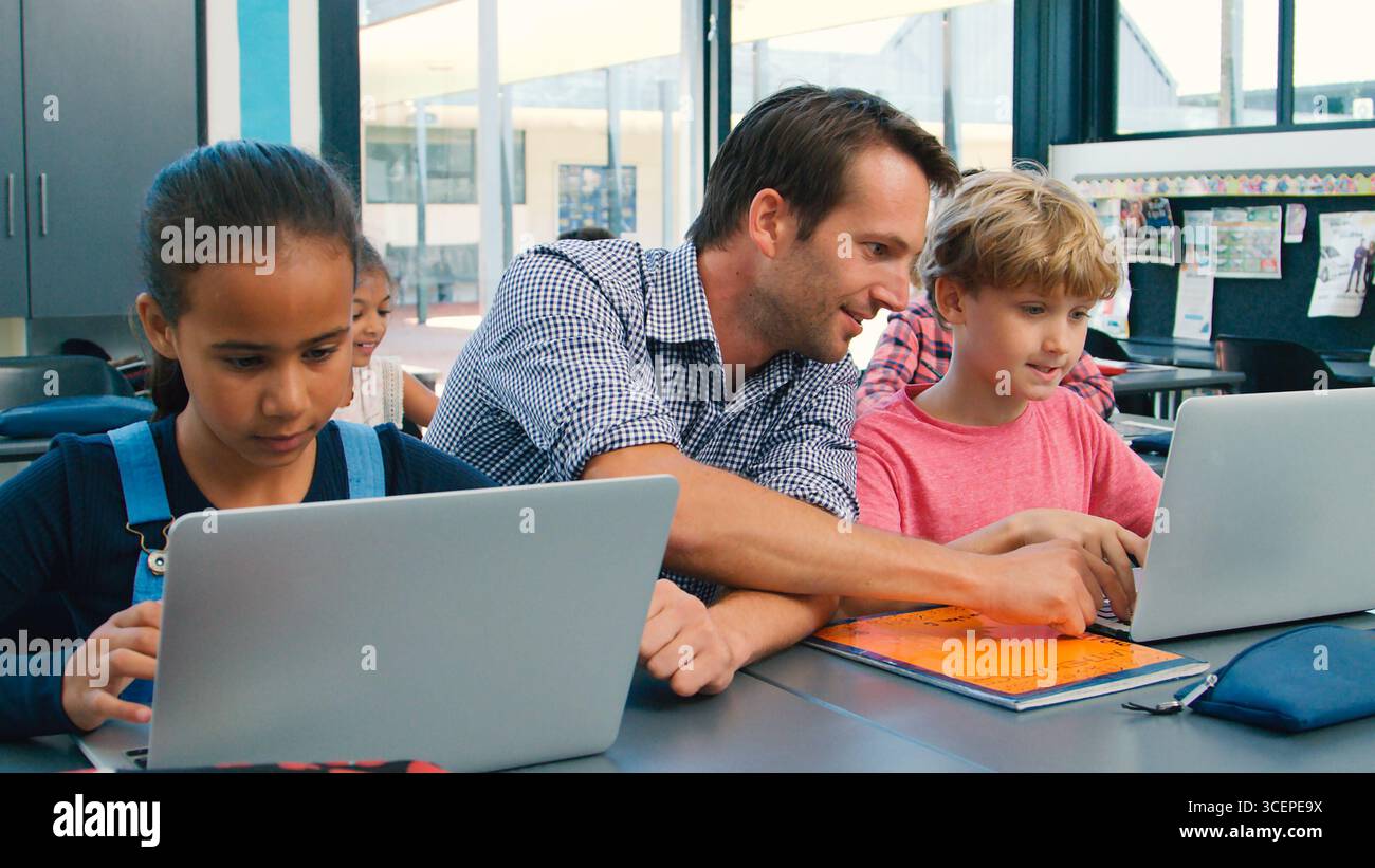 Male High School Teacher With Pupils Using Laptops At Desk In Technology Class Stock Photo