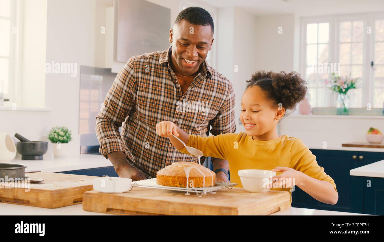 Family Shot With Father And Daughter Baking At Home In Kitchen Decorating Cake With Icing Stock Photo