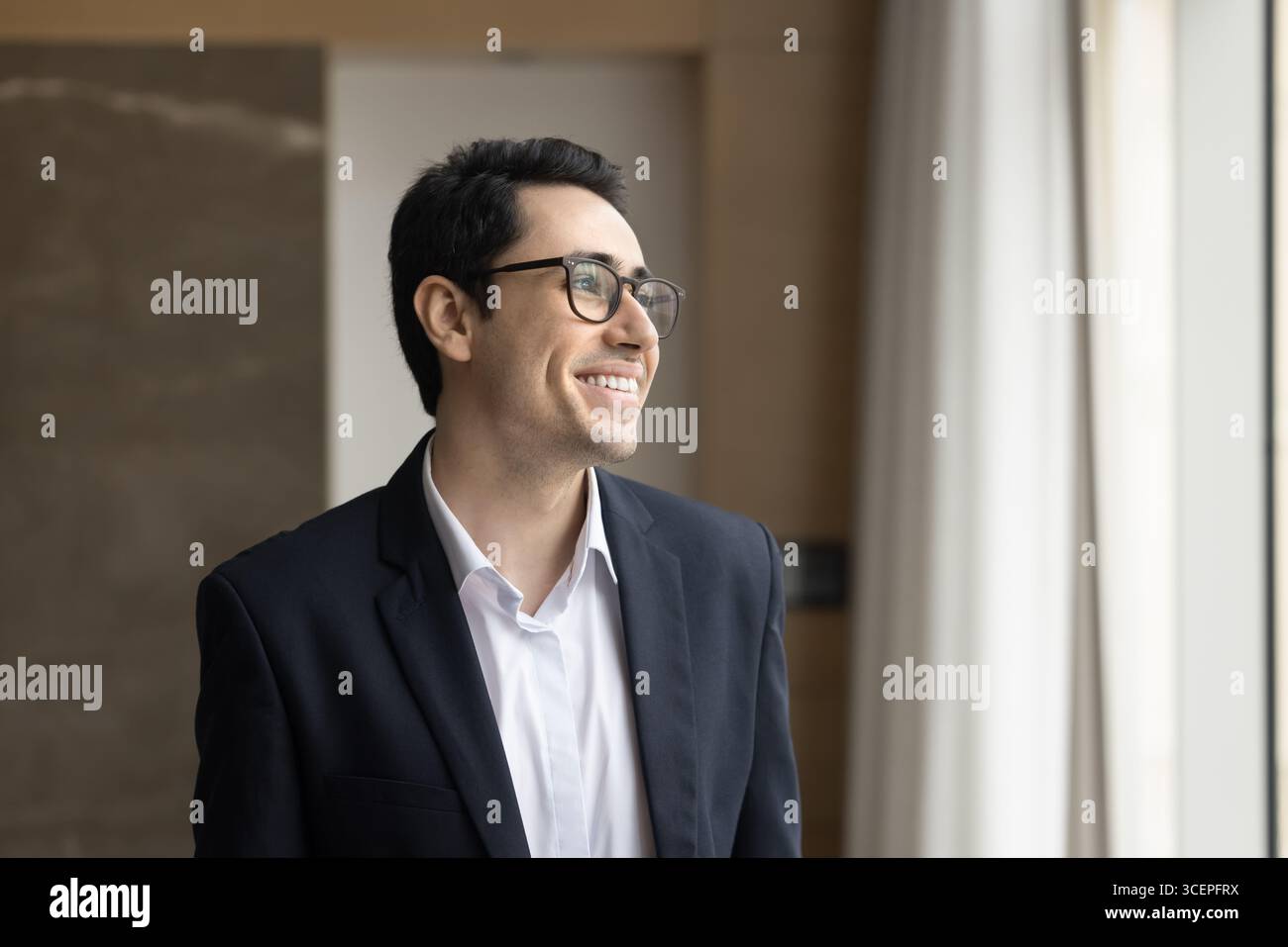 Portrait smiling young businessman standing by office window looking away Stock Photo