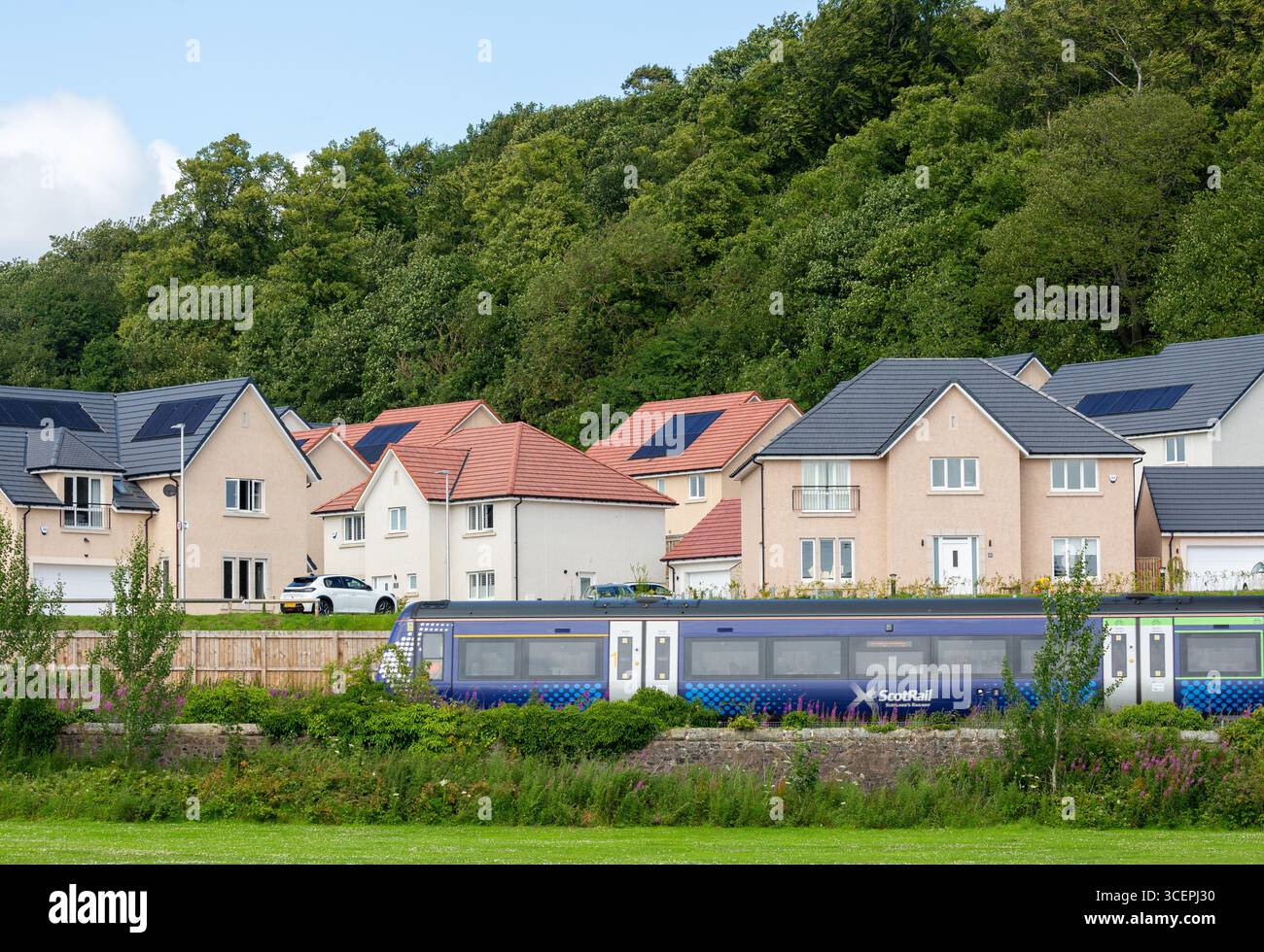 A train passing in front of a new housing development in Aberdour with the houses fitted with solar panels. Stock Photo