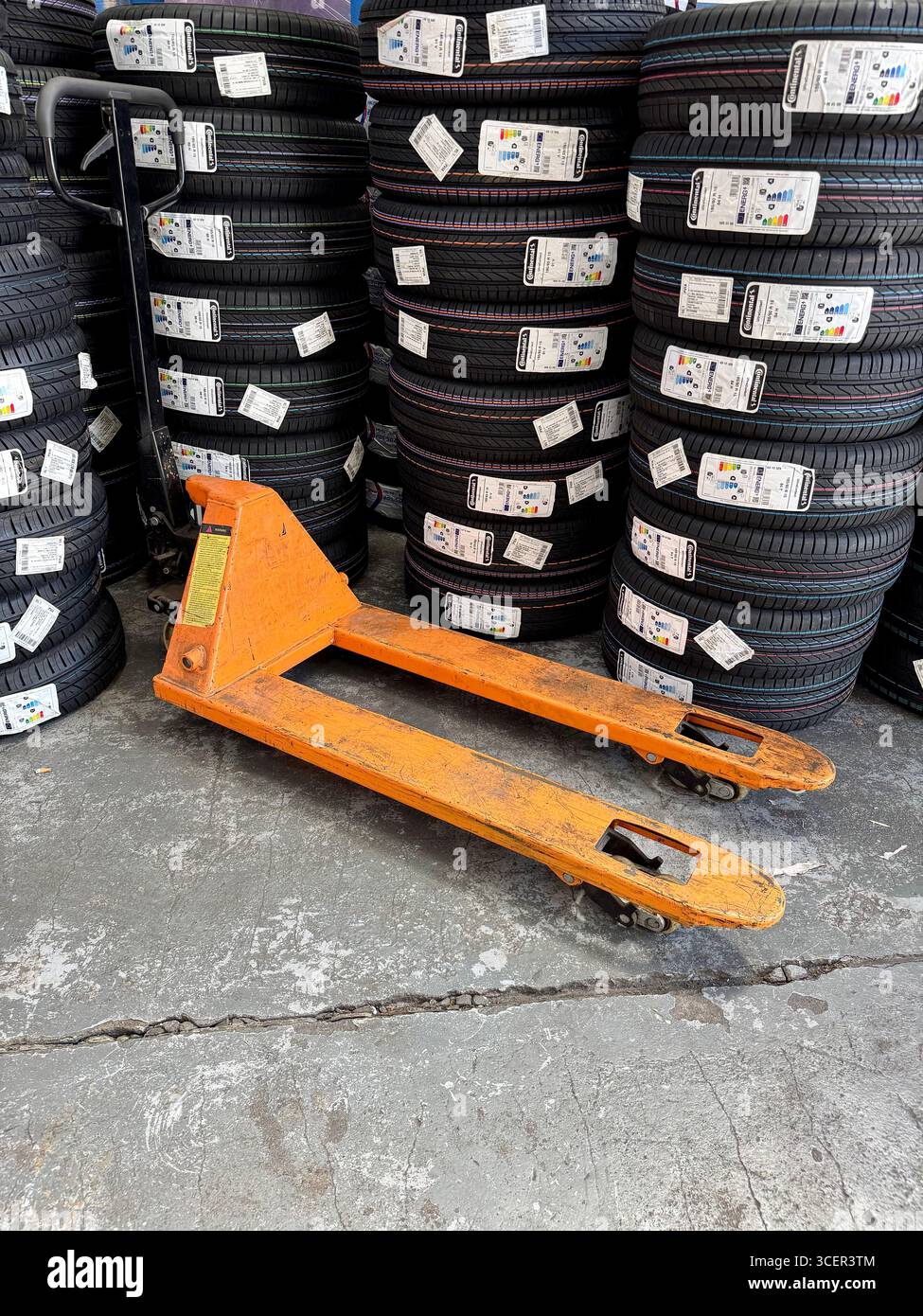 Stacks of new car tyres for sale in an automotive garage with an orange pallet jack. - Smartphone Captured Stock Image