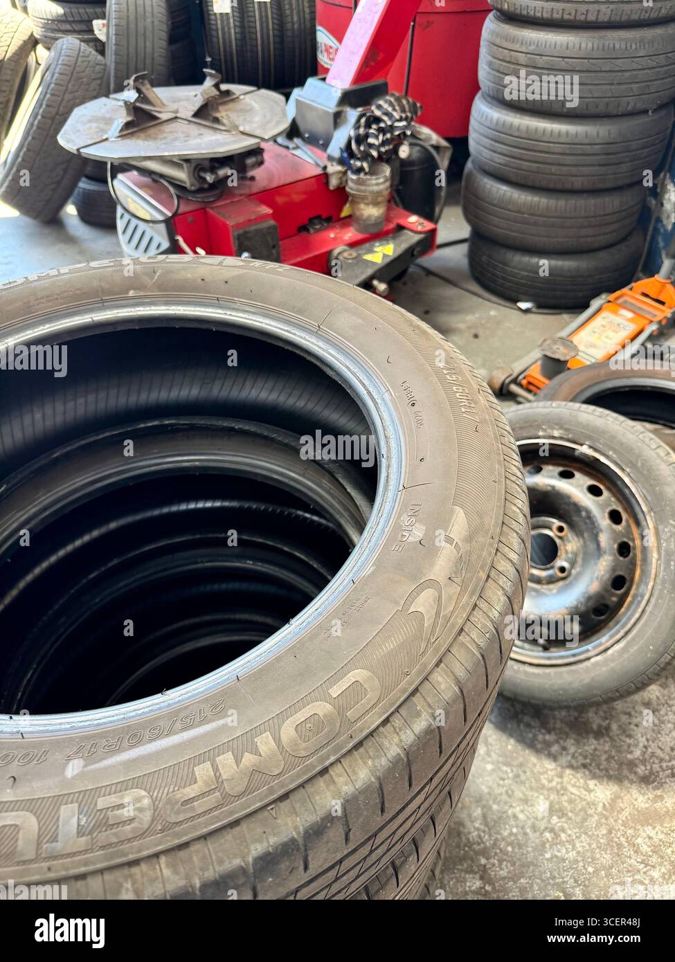 Car tyres and wheel rims inside an automotive workshop with tyre changing equipment. - Smartphone Captured Stock Image