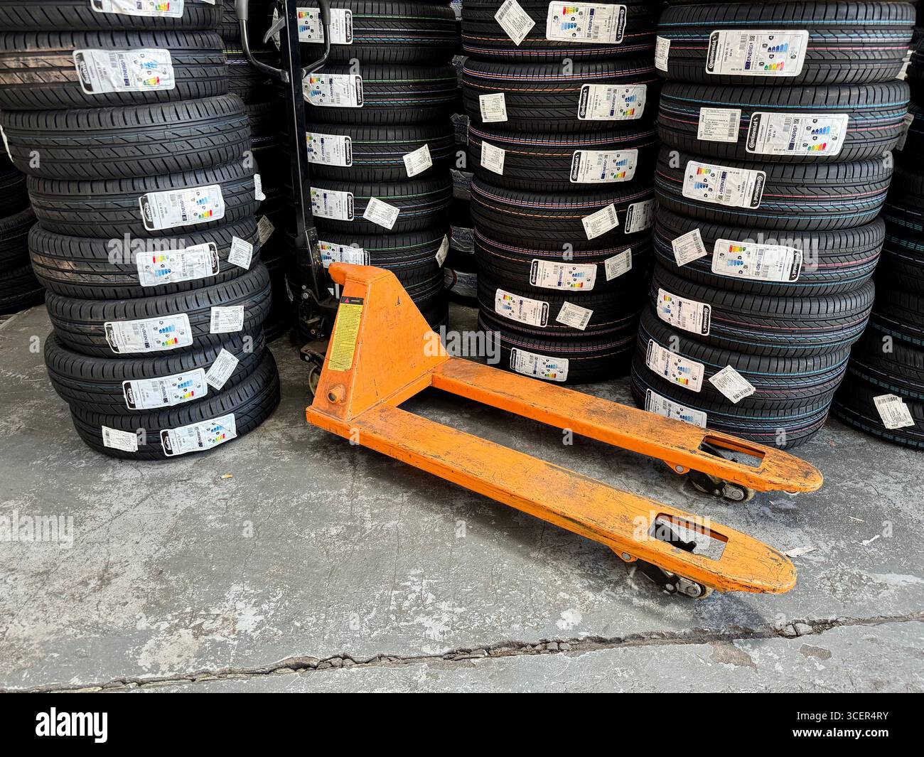 Stacks of new car tyres for sale in an automotive garage with an orange pallet jack. - Smartphone Captured Stock Image