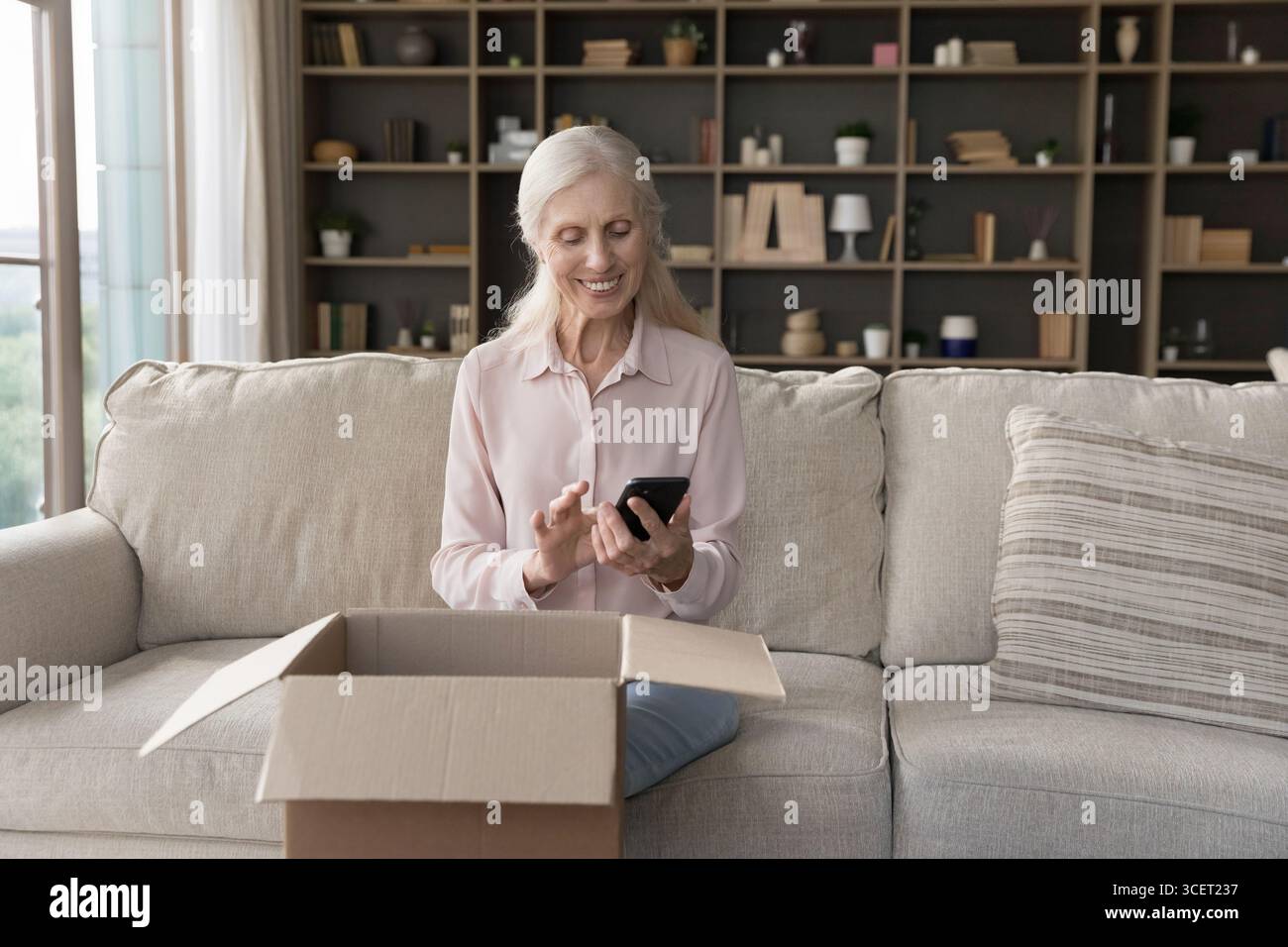 Elderly lady using smartphone sitting on sofa by opened delivery Stock Photo