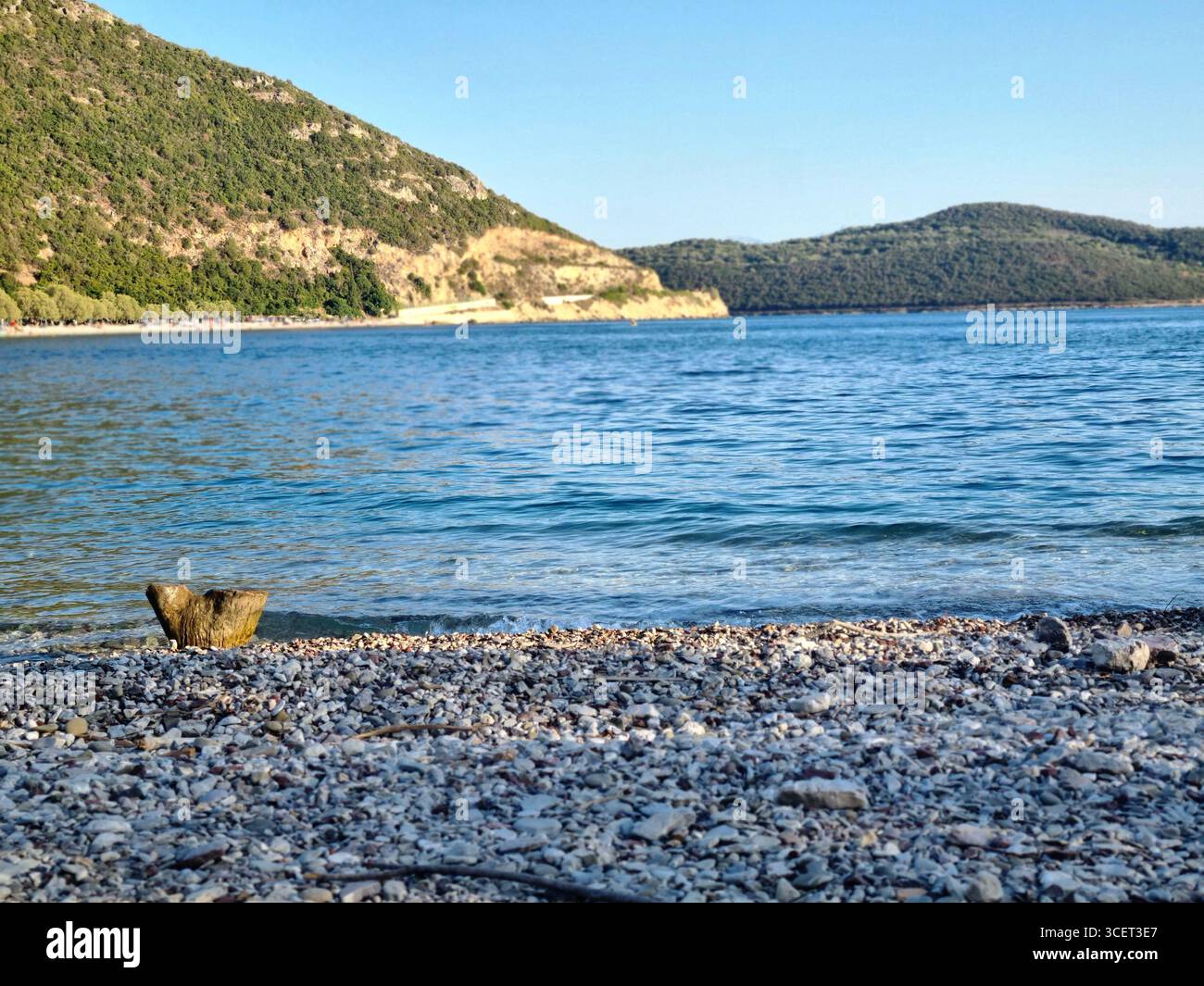 Rocky Beach with Clear Blue Sea and Green Hills in the Background - Smartphone Captured Stock Image
