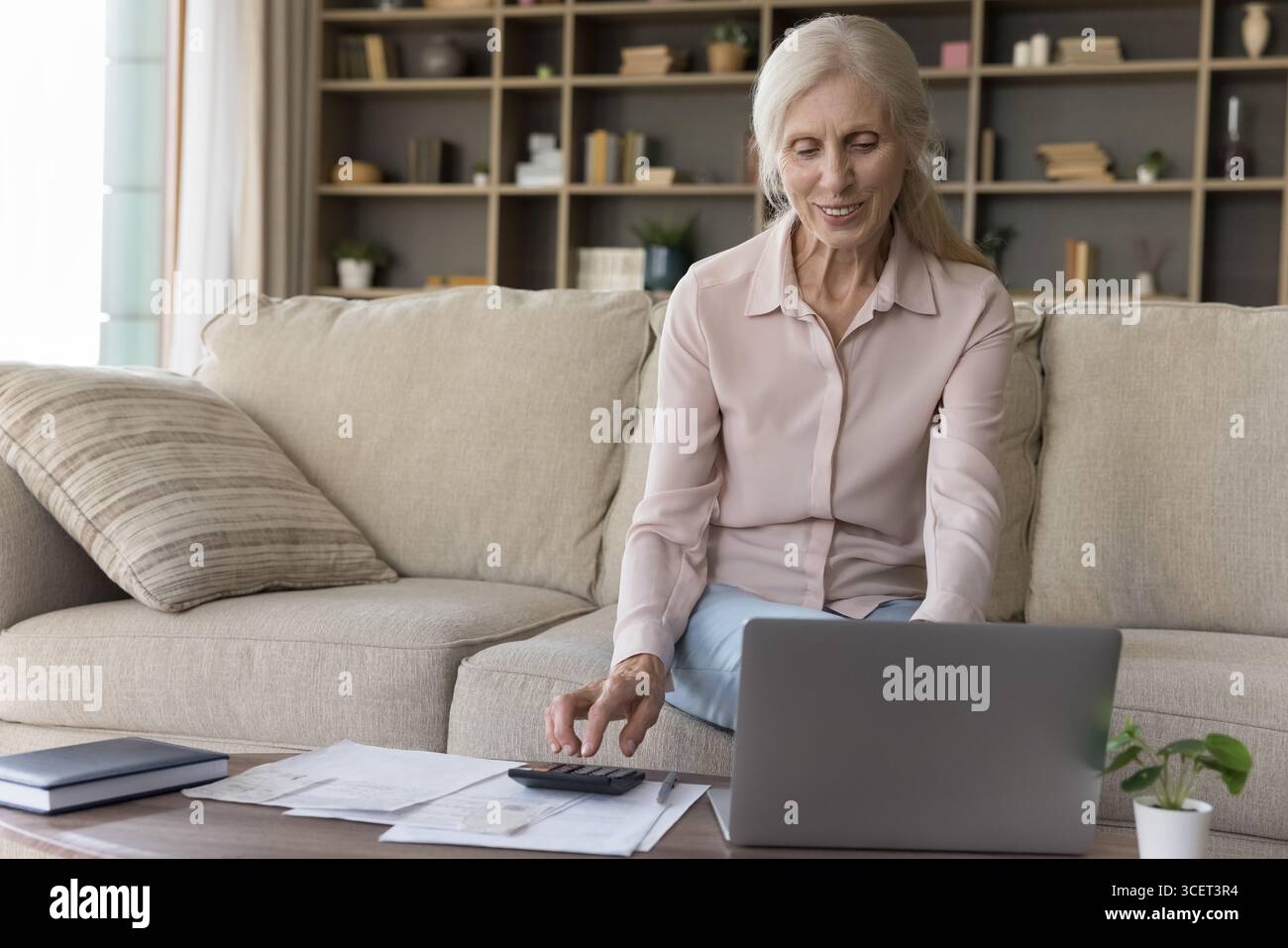 Smiling senior woman using computer printed statements to manage budget Stock Photo