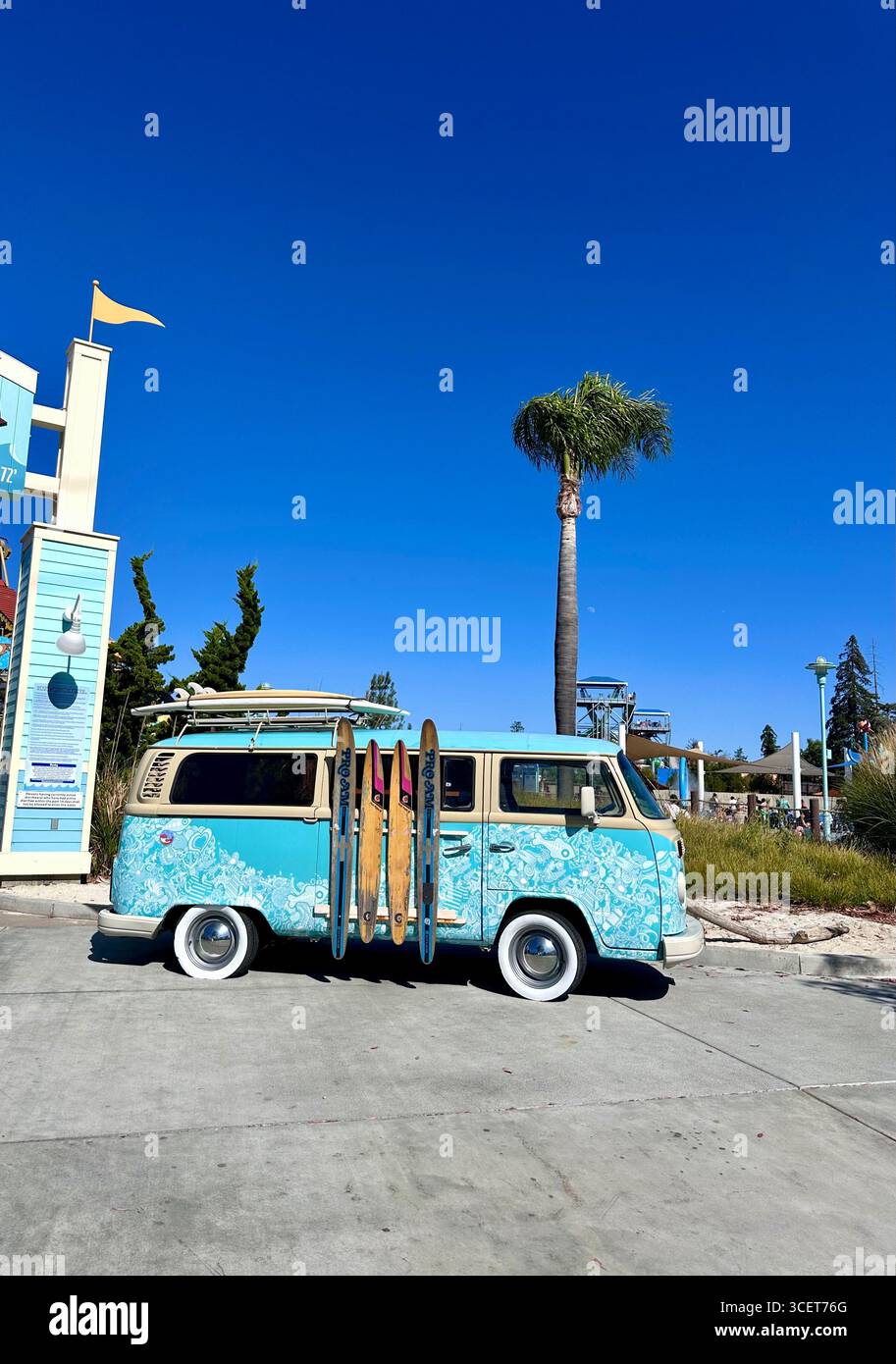 A retro Volkswagen camper van decorated with a surf-inspired design, parked with surfboards attached to the side at a beachside attraction, California - Smartphone Captured Stock Image