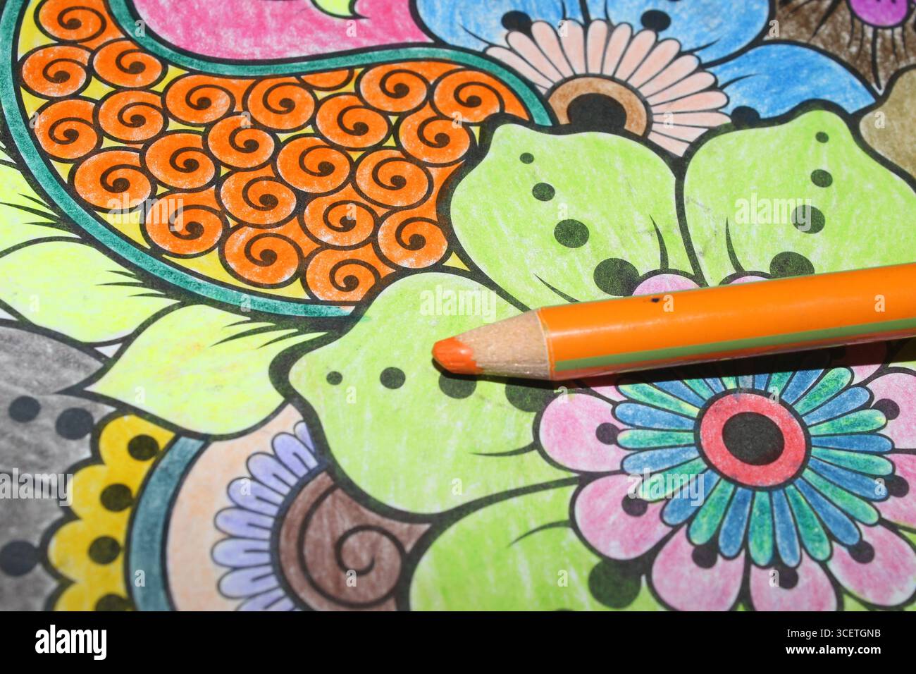 Orange colored pencil lying on a colored mandala drawing Stock Photo