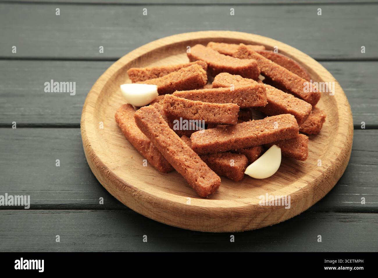 Tasty rye croutons on wooden plate on black background. Top view Stock Photo