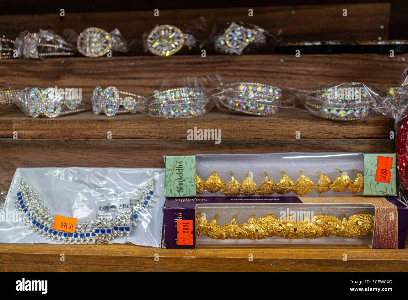 Shiny decorative bangles and necklaces displayed in packaging boxes on wooden background shelves Stock Photo