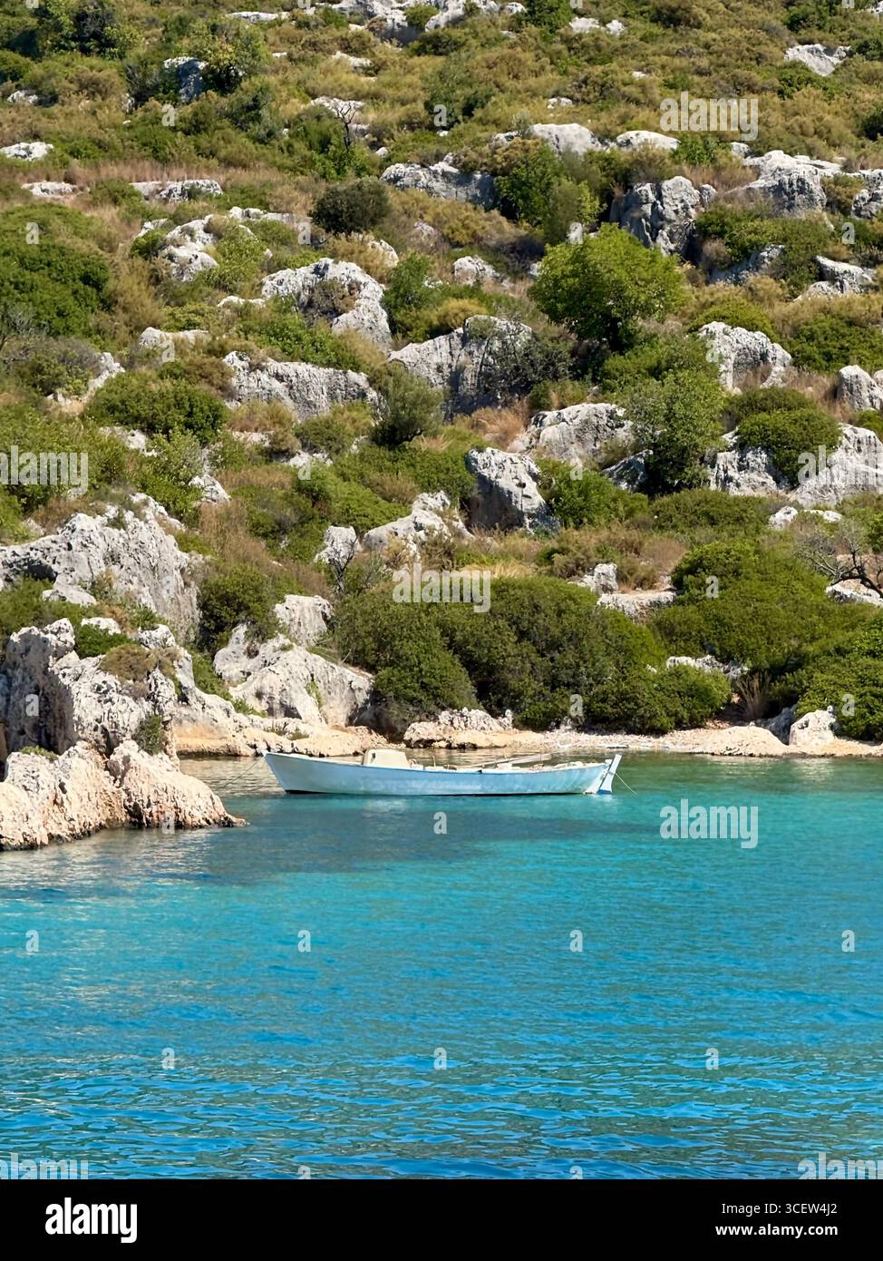 A lonely small wooden boat floating in a cozy turquoise bay surrounded by mountains. Scenic seascape, nature, perfect travel destination, and rest - Smartphone Captured Stock Image