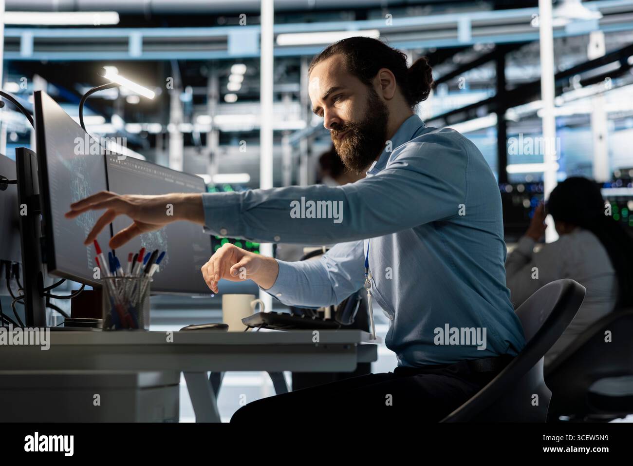 Engineer in data center using PC to update storage arrays software, configuring network virtualization. Man in server room using computer to verify settings, maintaining stable performance Stock Photo