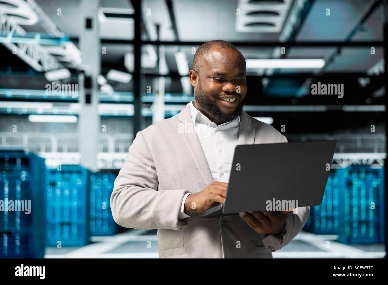 Smiling technician in data center workspace running system diagnostic tests and error checking utilities to fix problems. Happy employee looking for network issues affecting rigs performance Stock Photo