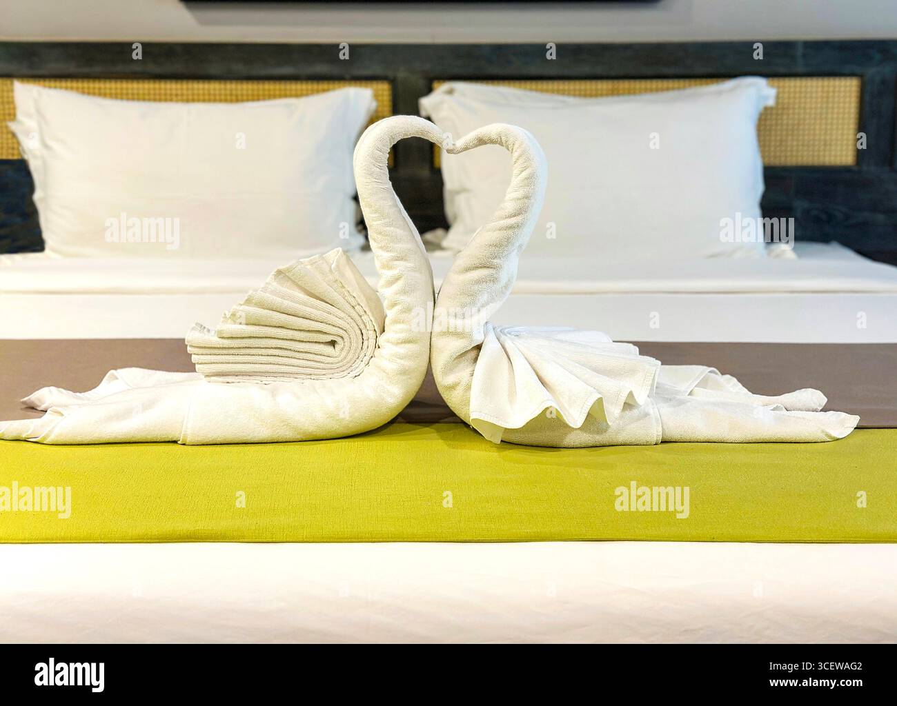 Two intricately folded white towel swans forming a heart shape, set elegantly on a hotel bed with a green runner Malacca malaysia - Smartphone Captured Stock Image