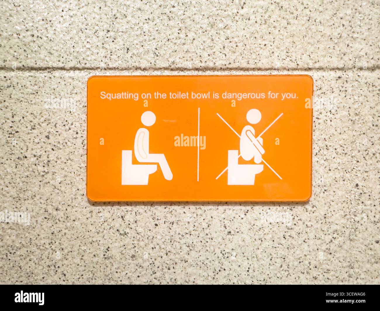 Orange warning sign with icon on restroom wall advising against squatting on toilet for safety Malacca malaysia - Smartphone Captured Stock Image