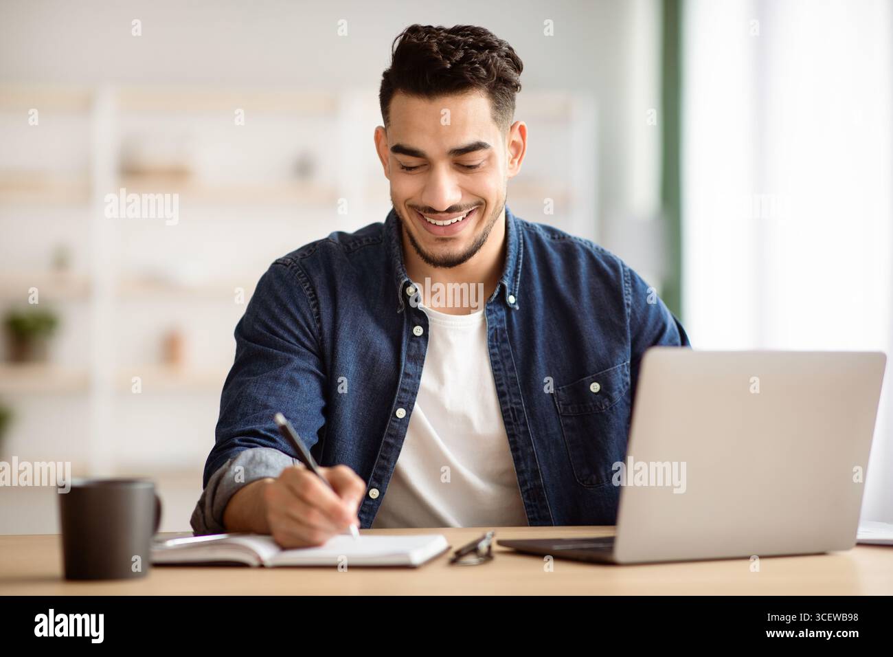 Joyful arab man taking notes while working with laptop Stock Photo