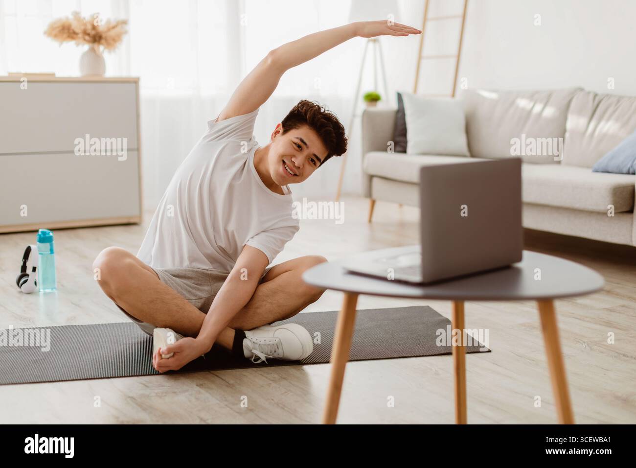 Asian guy doing stretching exercise watching online tutorial Stock Photo