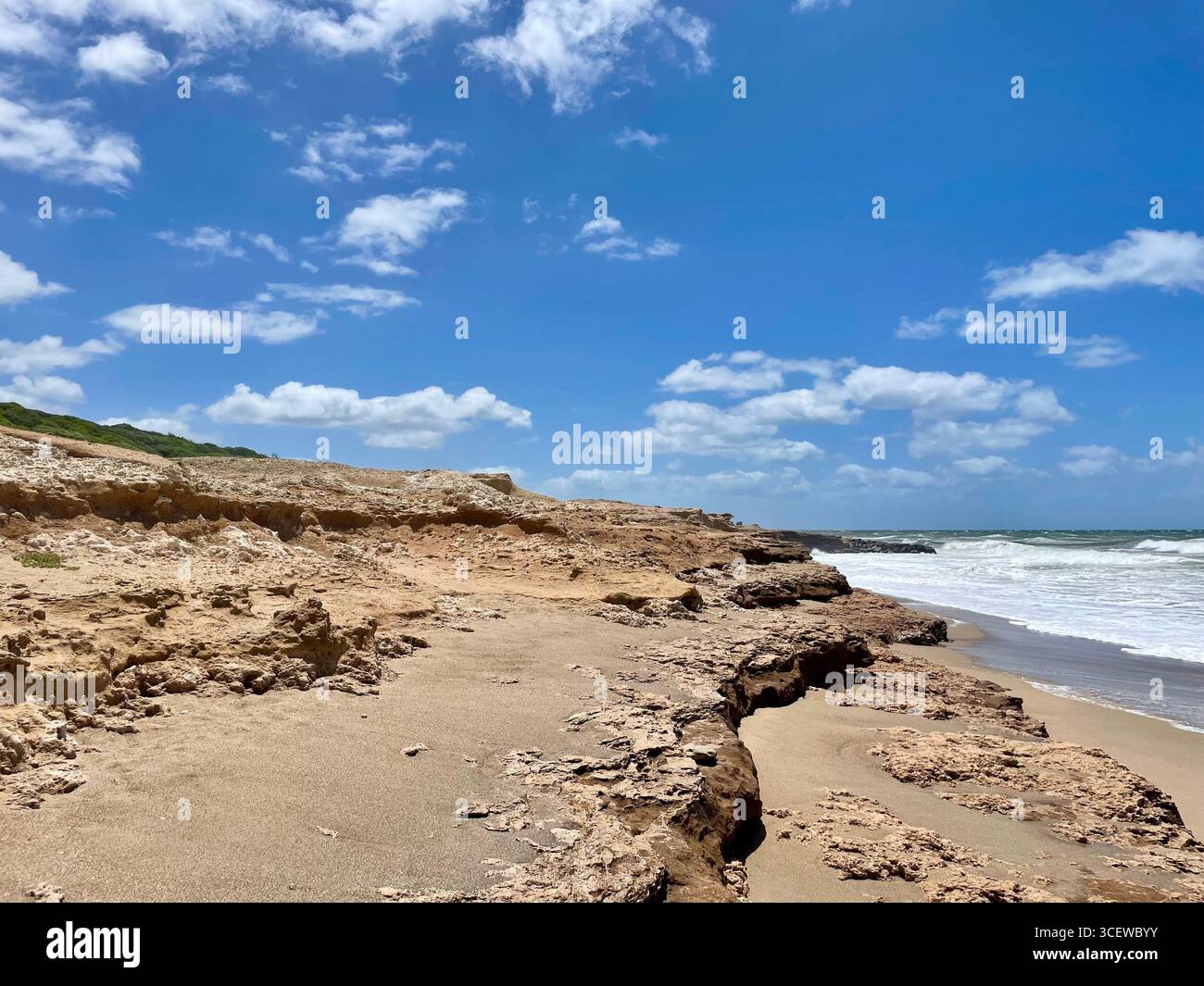 Rocky coastline with waves hitting the shore under a clear blue sky - Smartphone Captured Stock Image