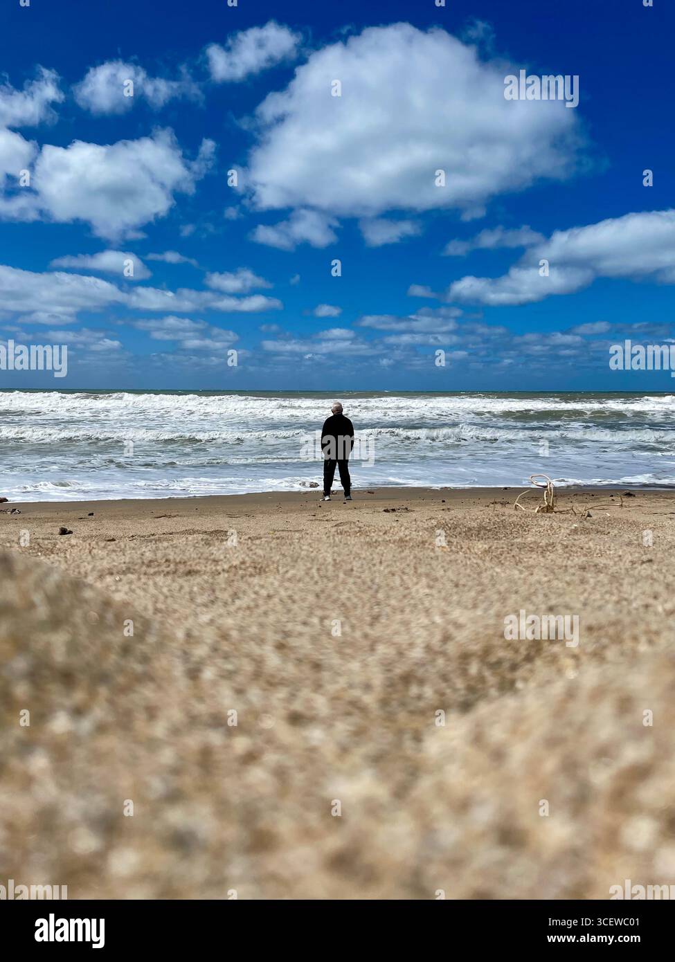 Person walking across a vast sandy beach under a clear blue sky. - Smartphone Captured Stock Image