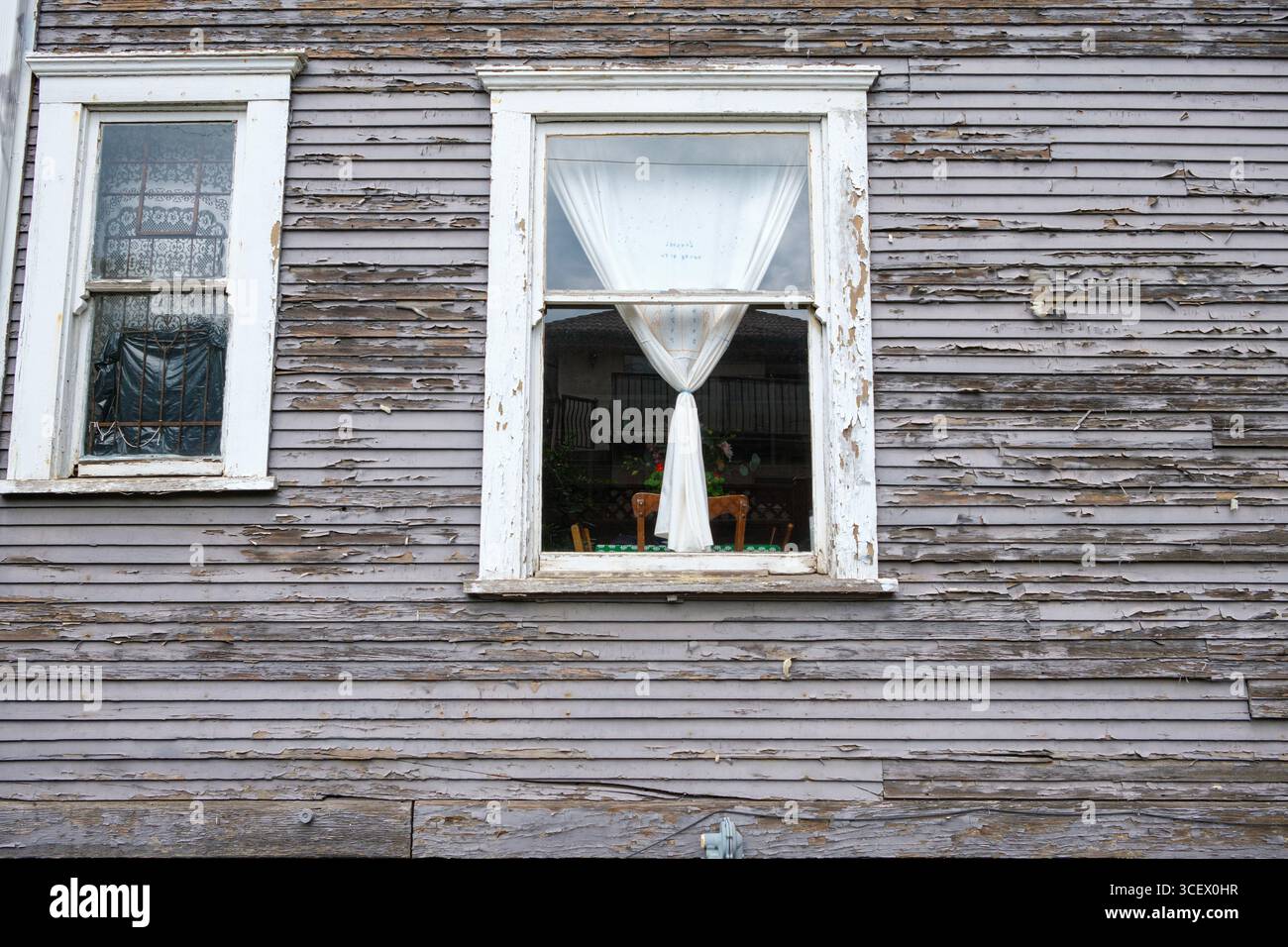 A weathered wooden house with peeling paint on the wall & windowsills ...