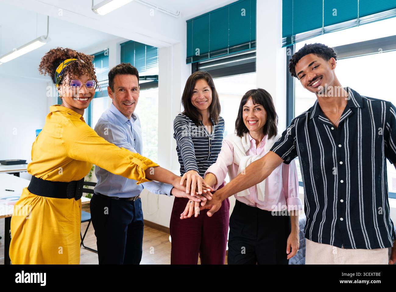 Five smiling colleagues joining hands in a modern office, celebrating teamwork and unity while demonstrating commitment to collaboration and project s Stock Photo