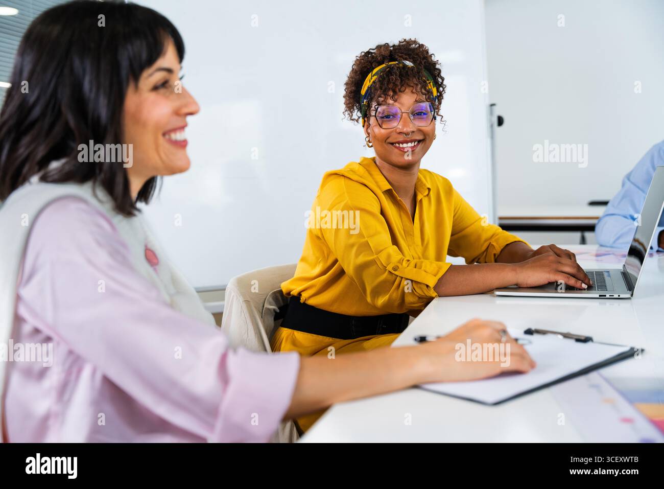 Two businesswomen are collaborating on a project, using a laptop and taking notes during a productive office meeting, showcasing teamwork and technolo Stock Photo
