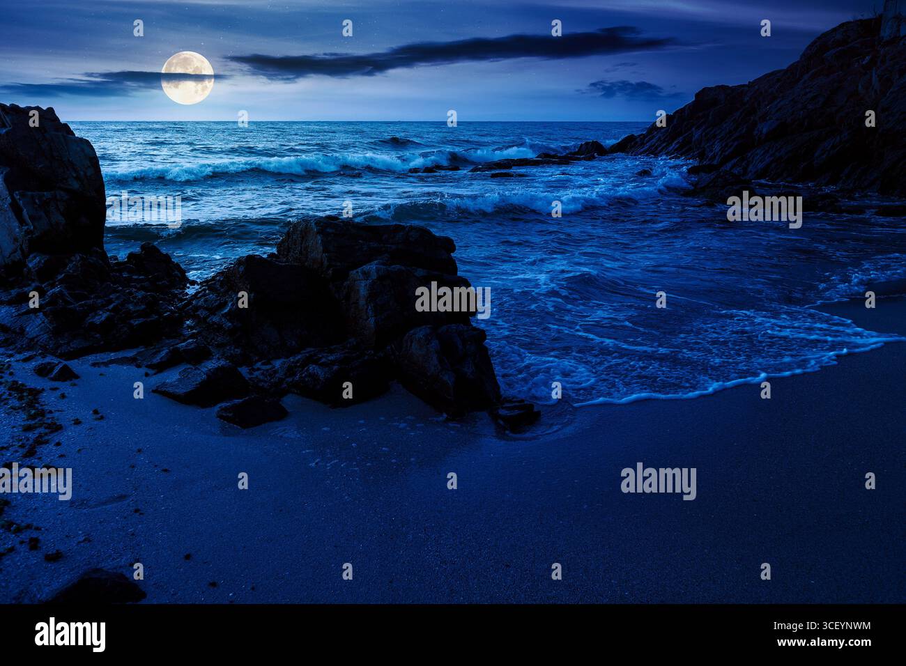 landscape by the sea at night in summer. beautiful beach with rocks washed by calm waves in full moon light. view to horizon under dark sky with cloud Stock Photo