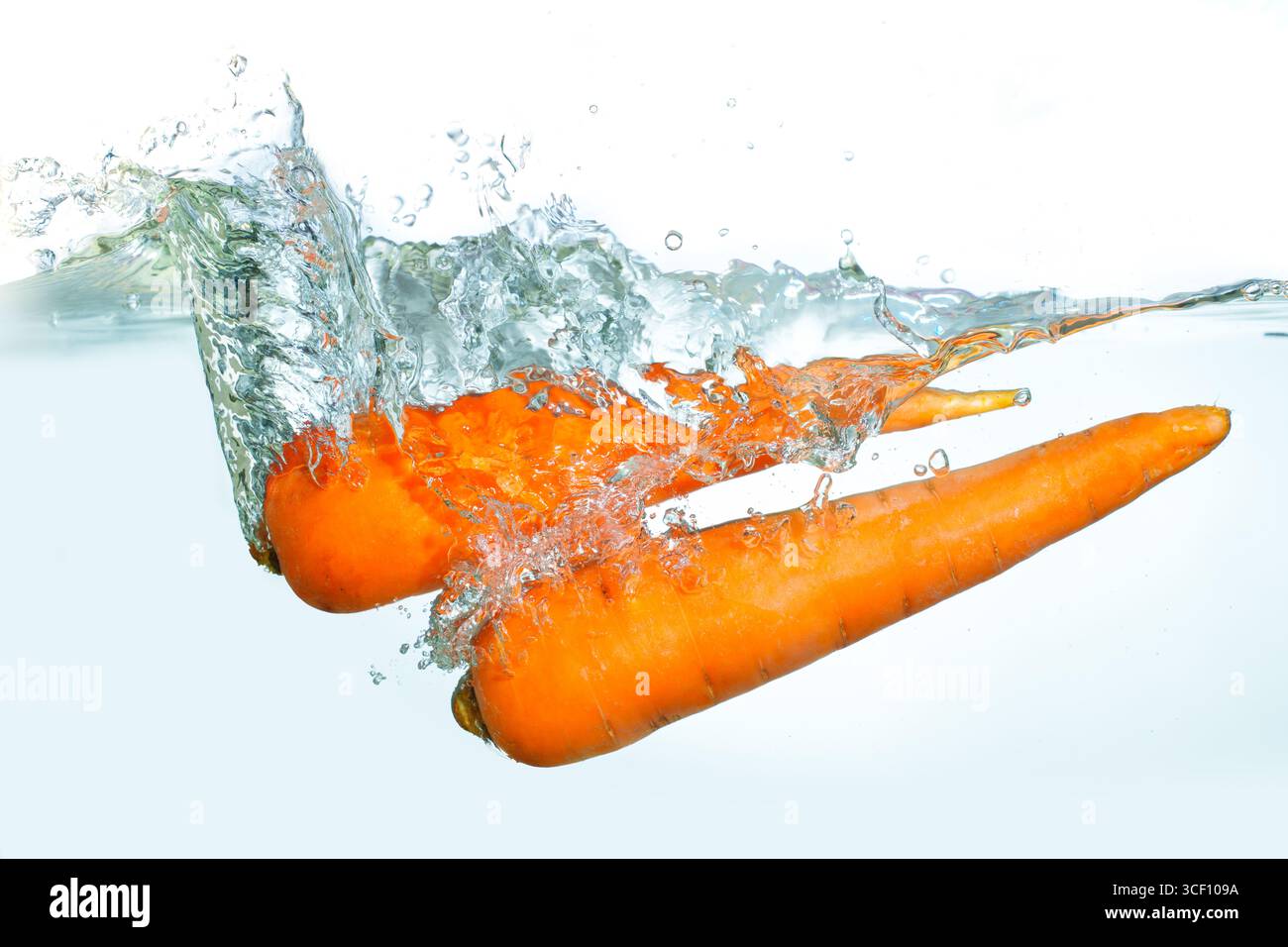 Dynamic splash of fresh carrots entering clear water, creating ripples ...