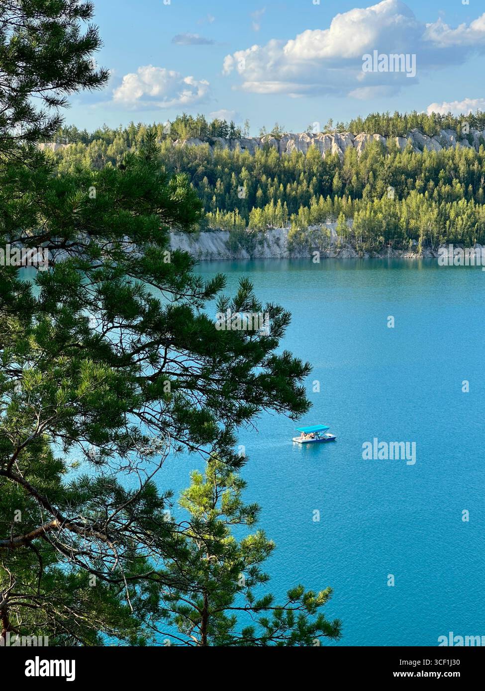 Scenic turquoise lake with boat and forested cliffs in summer. Beautiful landscape view of a turquoise blue lake with a small boat and green pine. - Smartphone Captured Stock Image