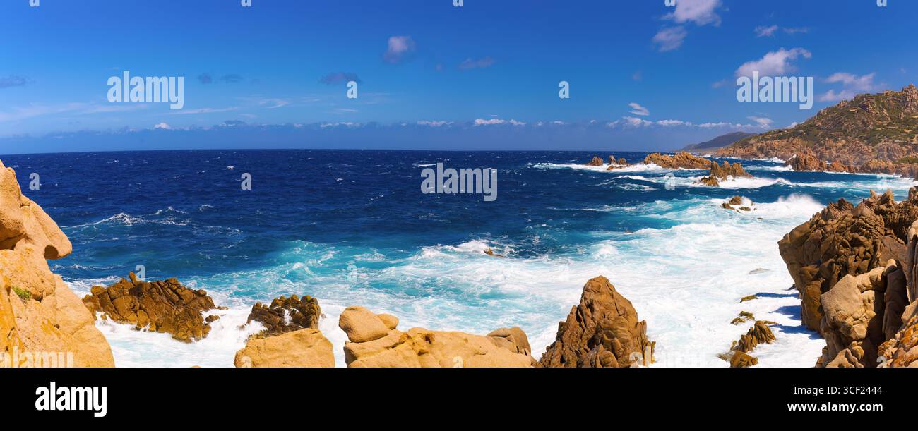Waves crash against rugged reddish rocks along the panoramic coastline ...