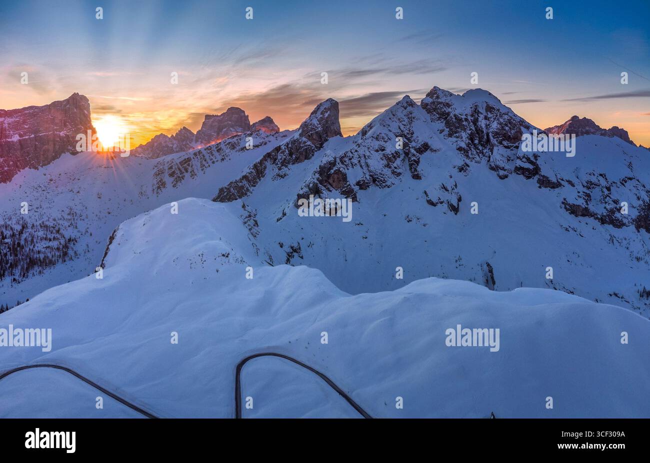 Aerial winter view of Passo Giau at dawn, with the sun rising behind Forcella Giau and Monte Cernera visible on the right. Snow-covered alpine slopes glow in the early morning light. Dolomites, Colle Santa Lucia municipality, Belluno province, Veneto region, Italy Stock Photo