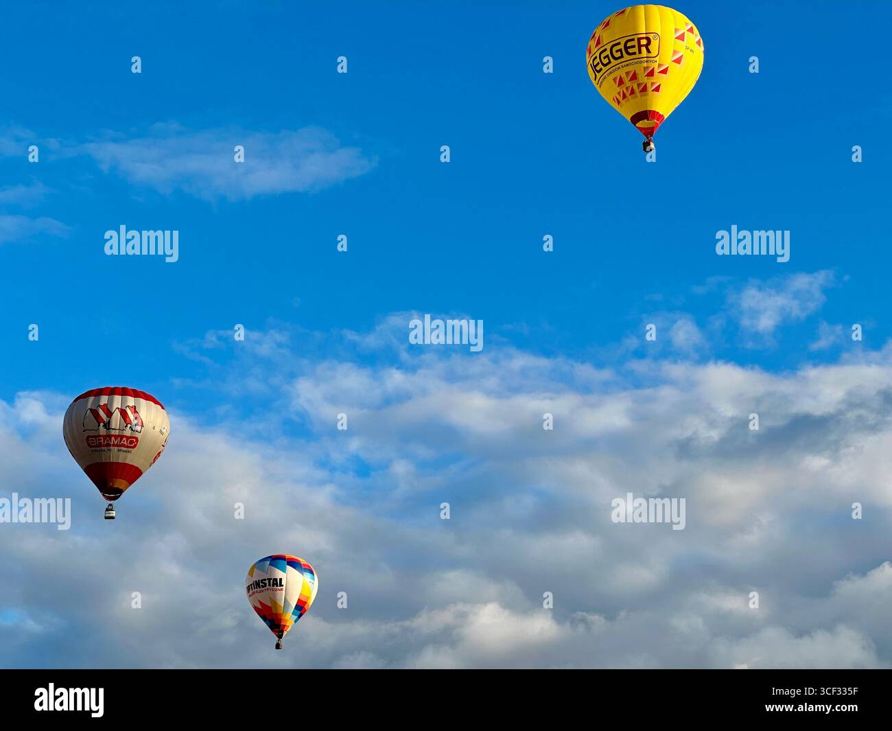hot air balloons floating in blue sky with scattered clouds. Egger and Cristal balloons during festival. - Smartphone Captured Stock Image