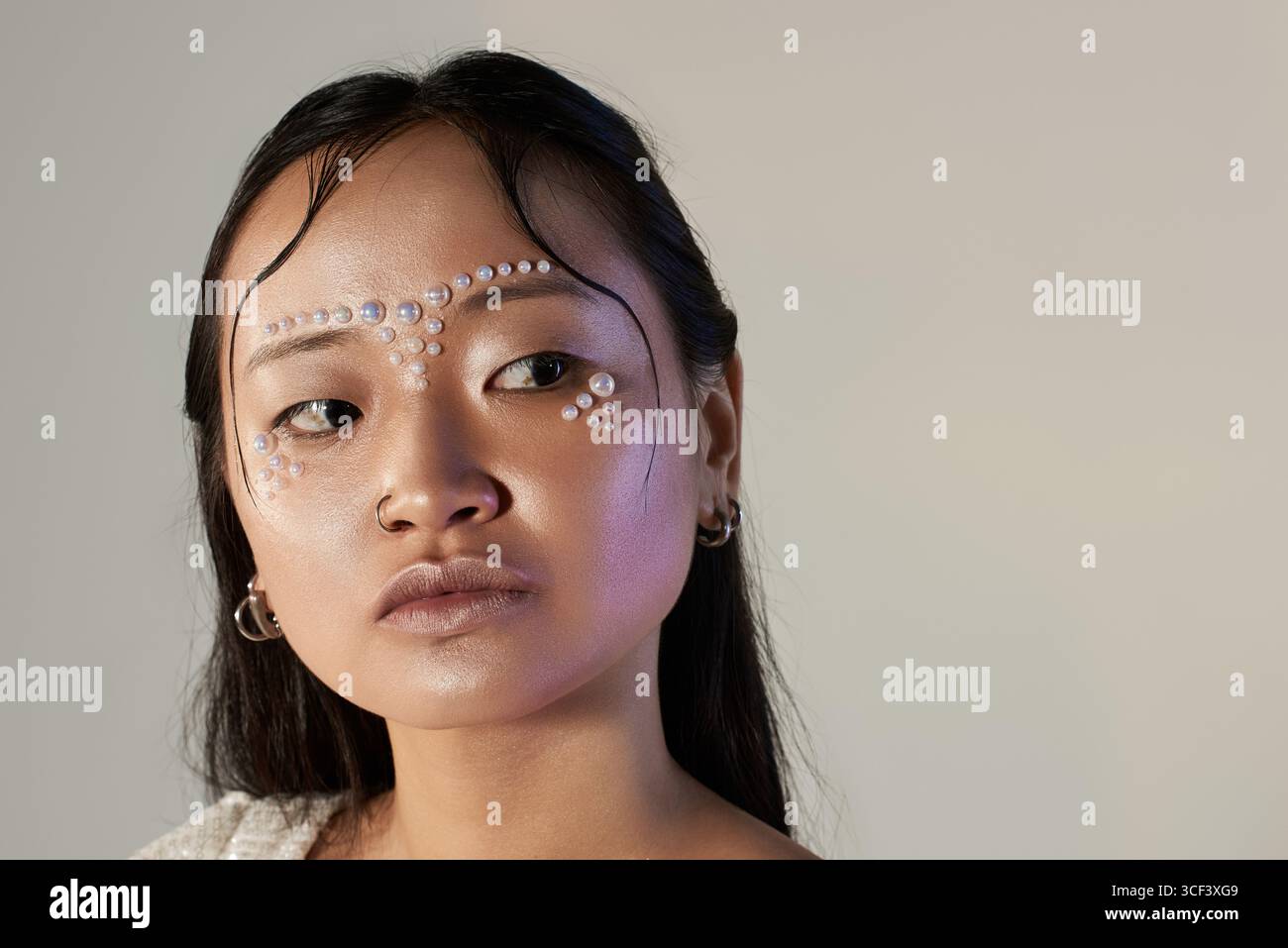 A young Asian woman showcases stunning creative makeup adorned with pearls on her face in a studio. Stock Photo