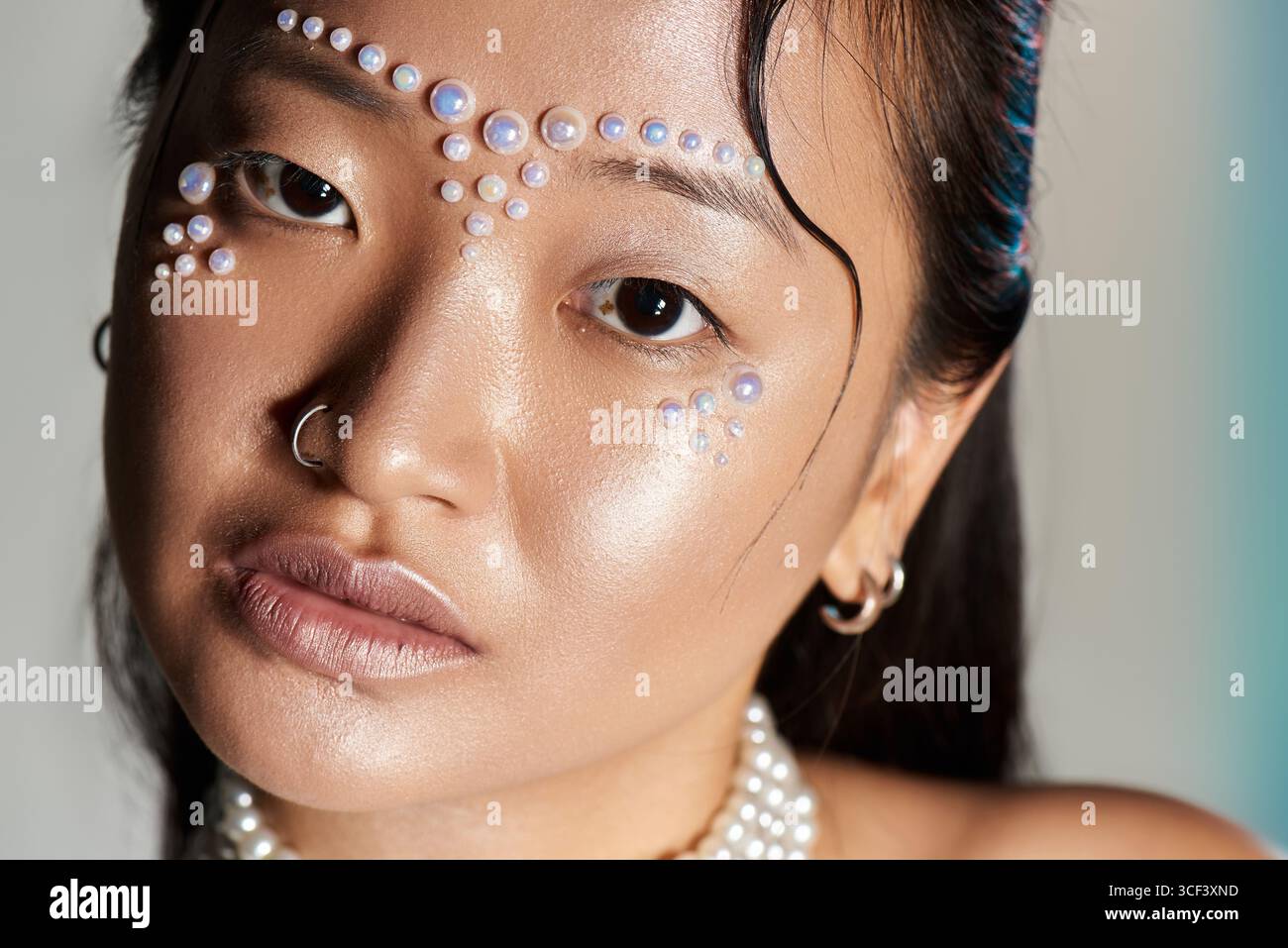 A talented young Asian woman showcases innovative makeup with pearls adorning her face in a studio. Stock Photo