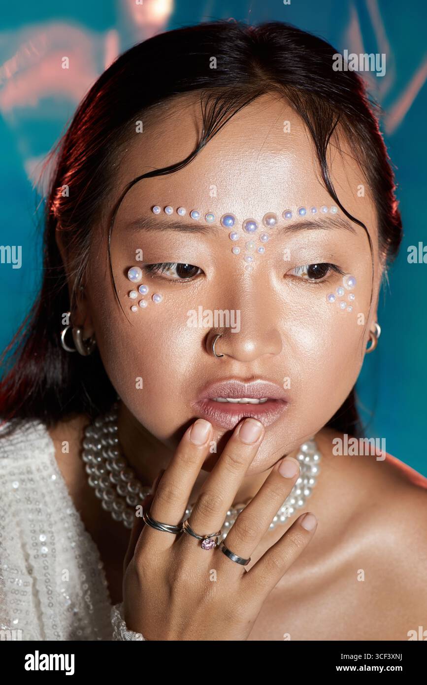 An Asian young woman showcases an artistic makeup look featuring pearls on her face in a studio. Stock Photo
