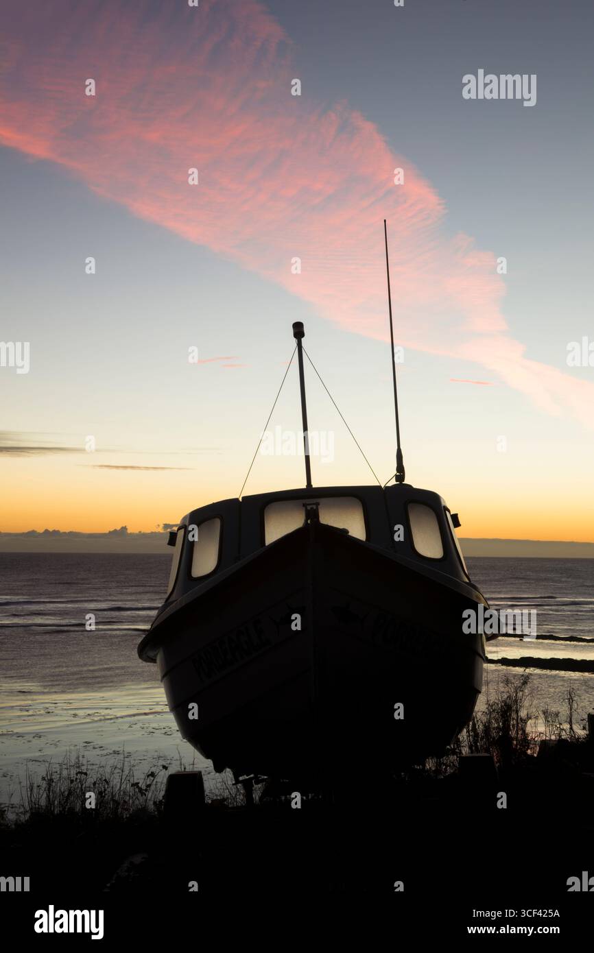 Silhouette of a boat out of the water and fixed to a trailer at daybreak in the coastal village of Robin Hood's Bay - Stock Image