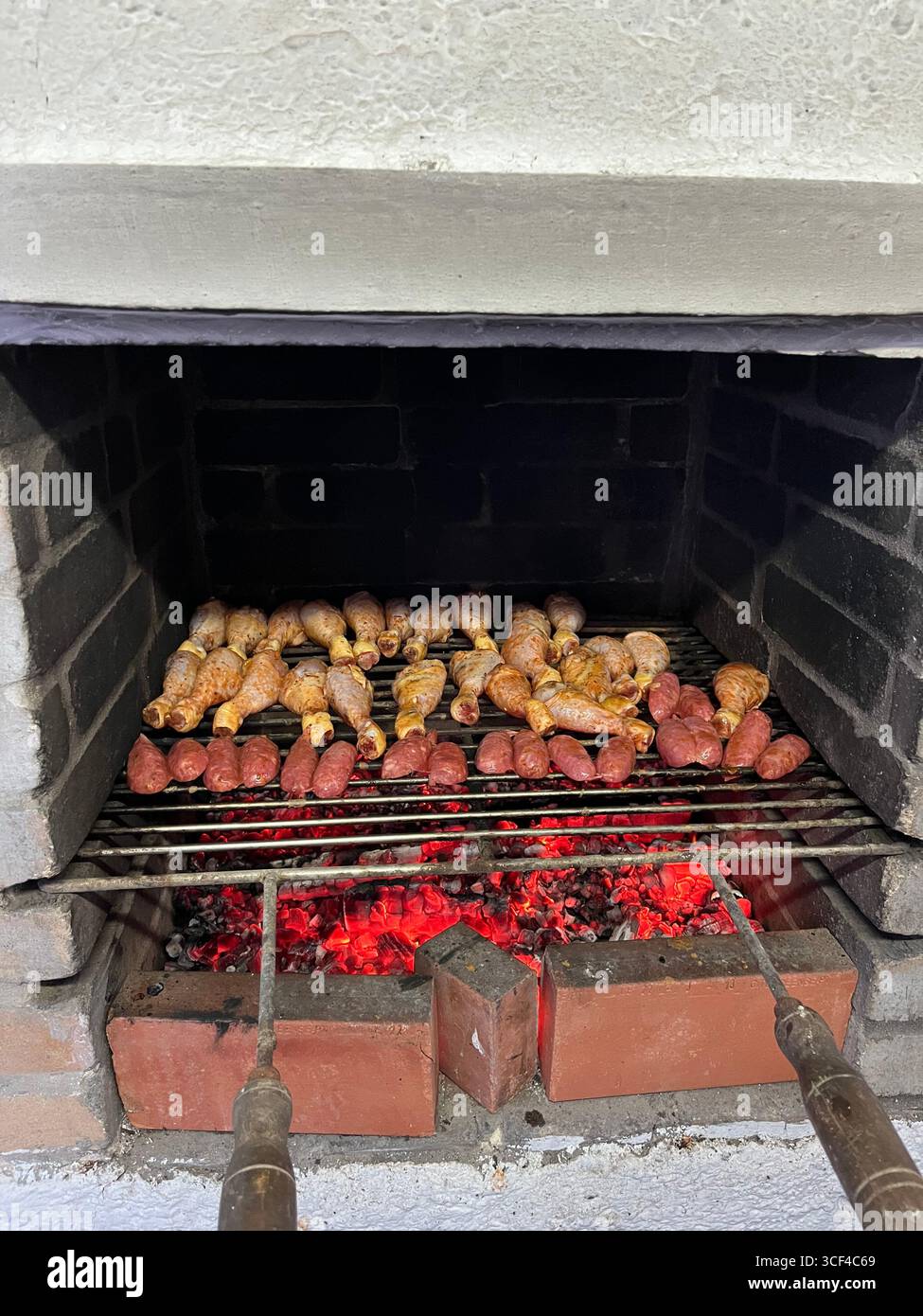 Sausages and chicken pieces grilling over hot charcoal embers on a traditional barbecue. - Smartphone Captured Stock Image