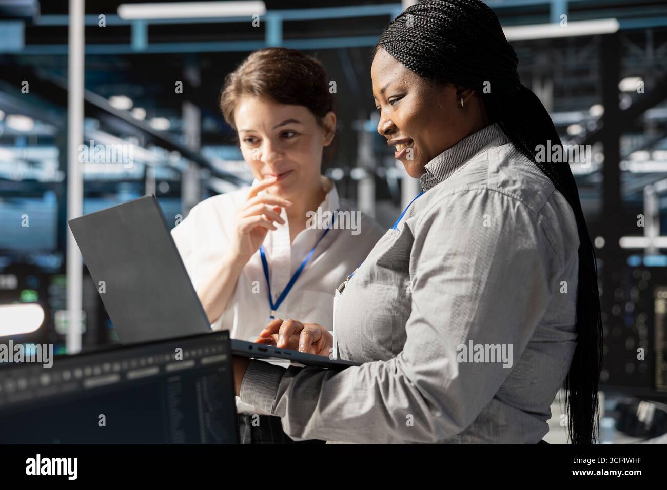 Smiling engineering team using laptop in data center, managing server virtualization, running scripts. Happy coworkers using programming language on notebook in server farm Stock Photo