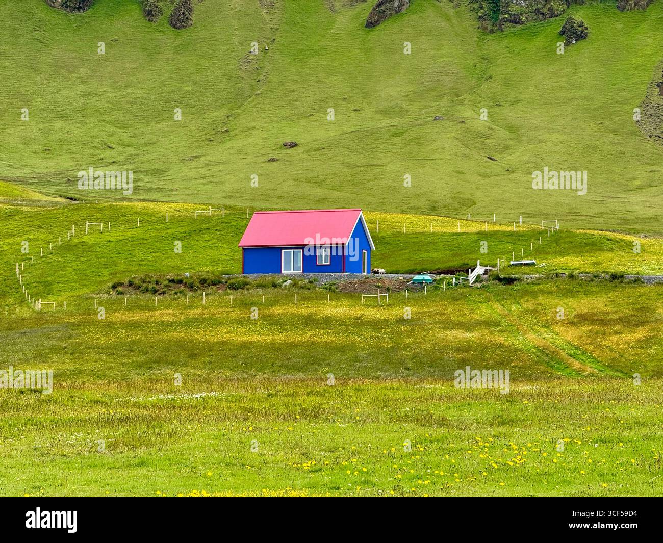 Blue house, with dark pink roof stands out amongst the grassy field and hill. - Smartphone Captured Stock Image
