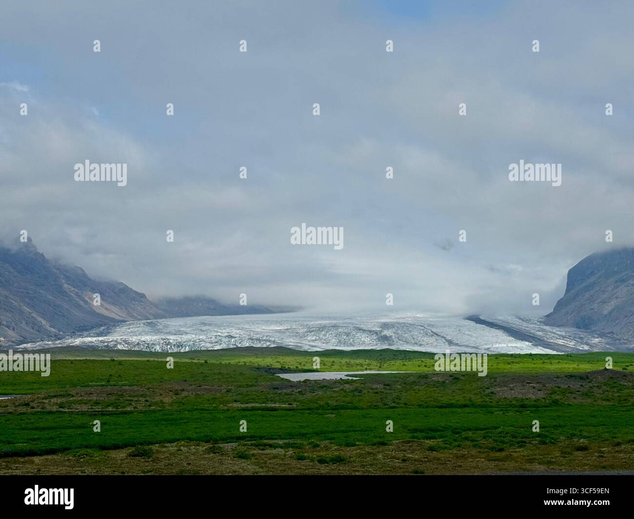Beuatiful landscape with Skaftafell glacier appears to be spilling out into a green field from between 2 small mountains in summer. - Smartphone Captured Stock Image