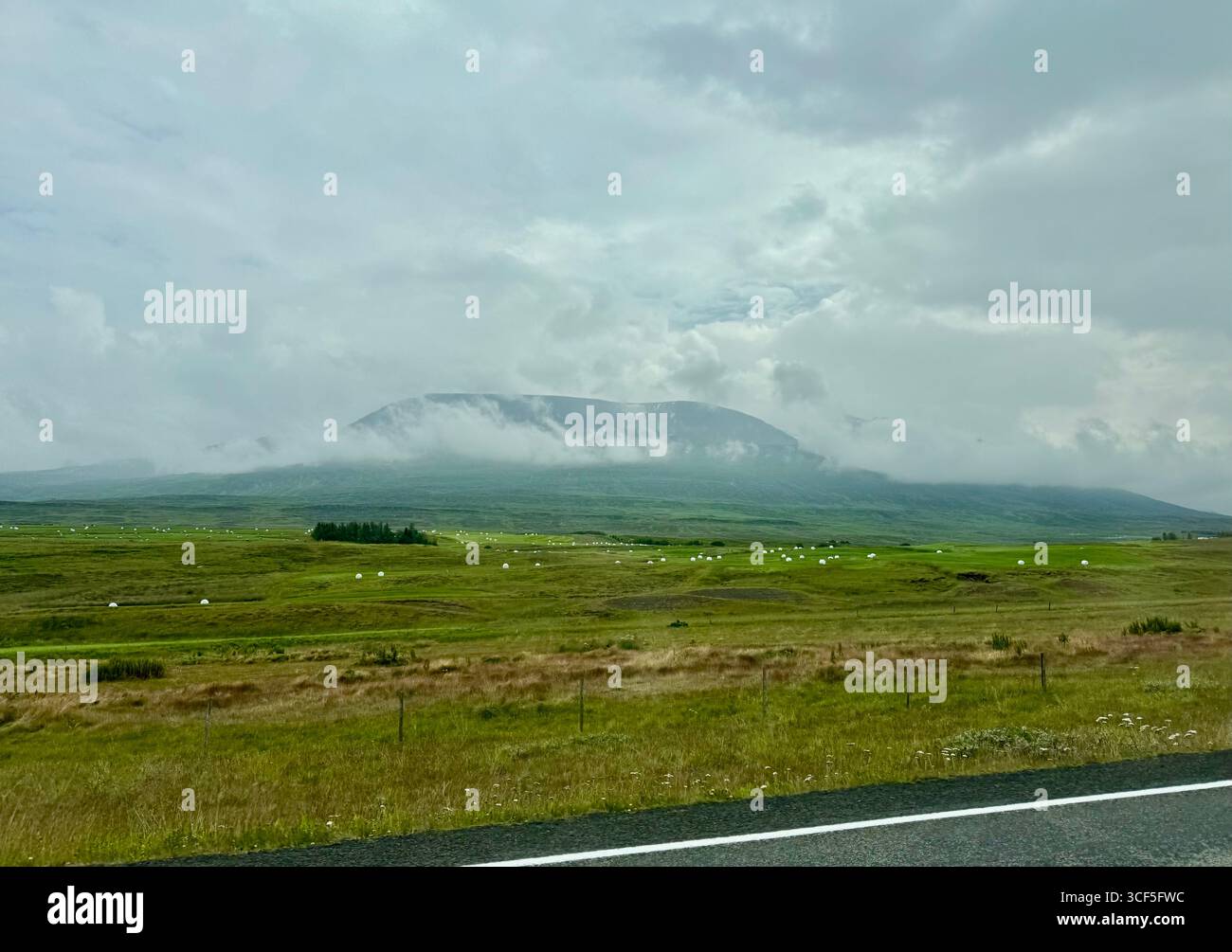 View of Hlidarfjall mountain with clouds and fog descending on top it, taken from the ring road area in Horgarsveit, north Iceland. - Smartphone Captured Stock Image