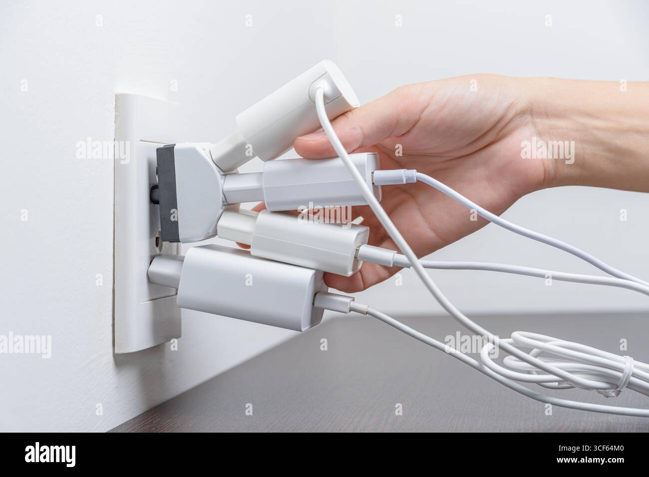 Hand inserting electrical plugs into outlet. Electrical overload Stock Photo