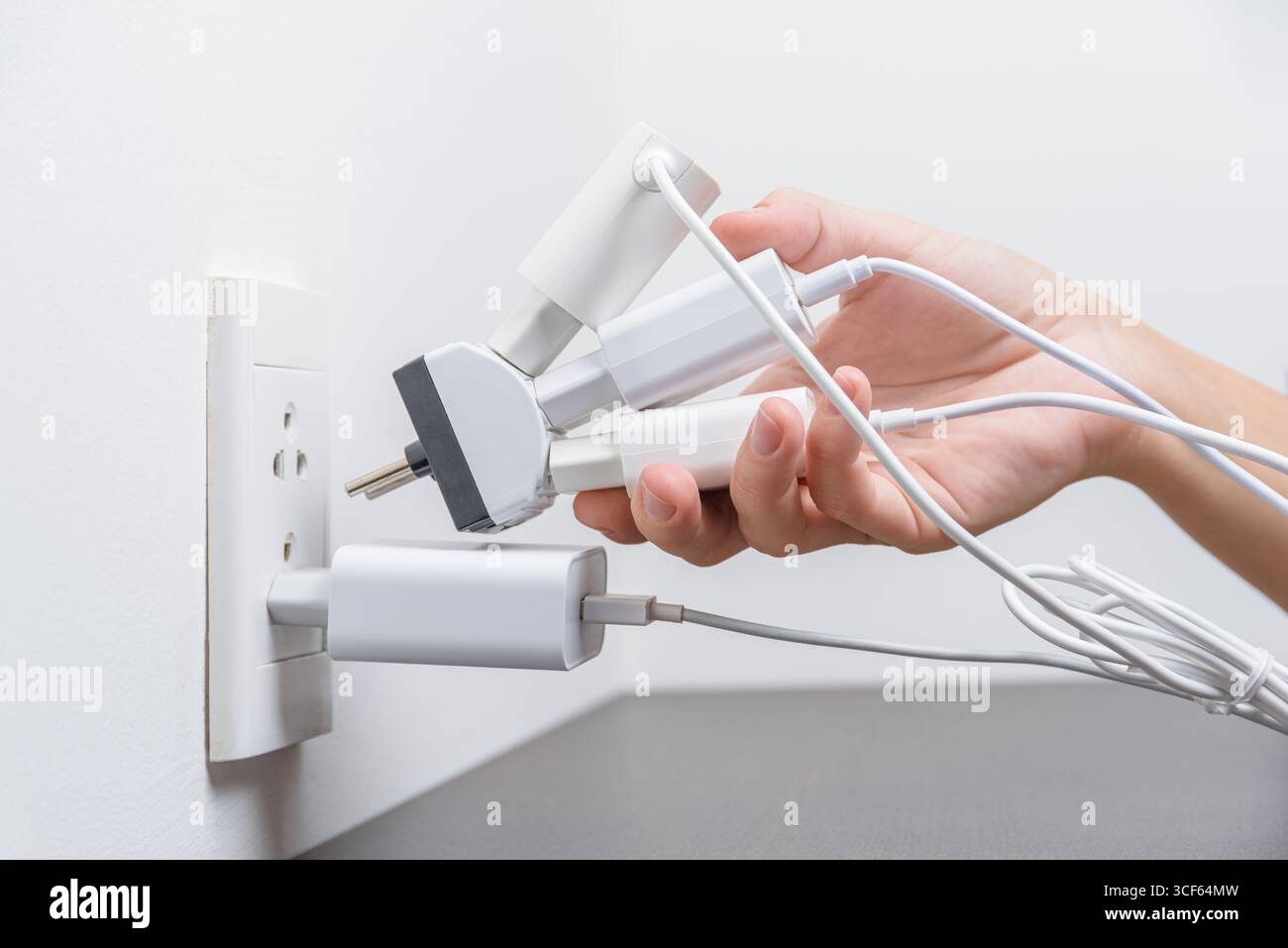 Hand inserting electrical plugs into outlet. Electrical overload Stock Photo