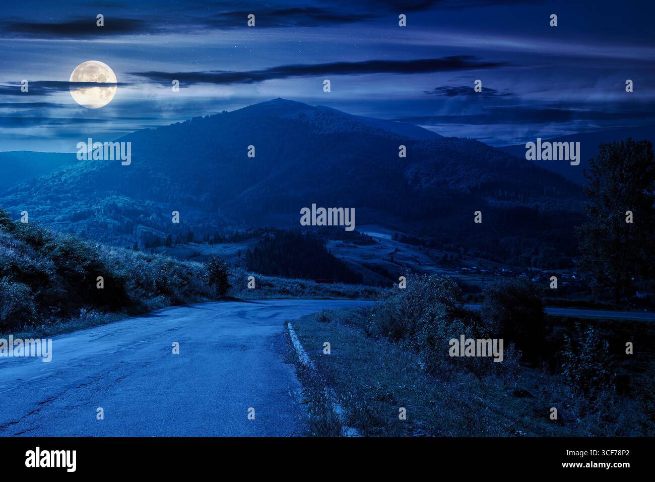 mountain pass at night. asphalt road winding down the hill. countryside scenery with valley in front of mountain peak under cloudy sky in full moon li Stock Photo