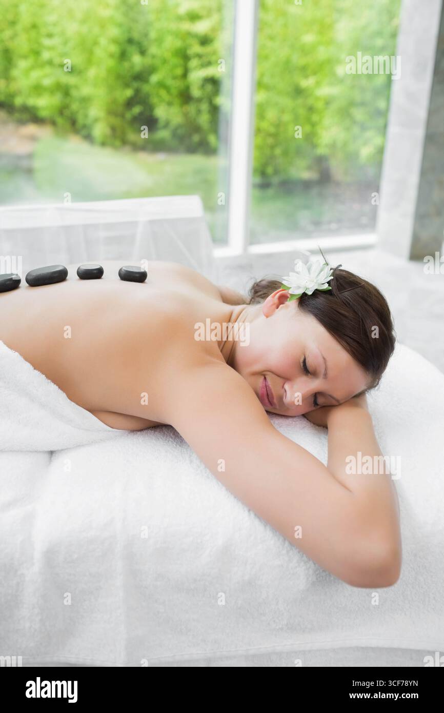 Female receiving hot stone massage on massage table in spa with flower in hair, copy space Stock Photo