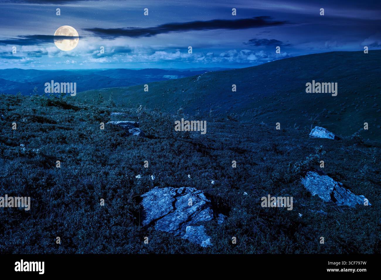 mountain landscape in summer at night. beautiful view of rolling green hills and alpine meadows in full moon light. scenery with clouds on the dark sk Stock Photo