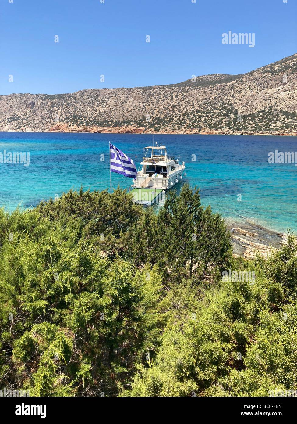 A small yacht moored off a dreamy Greek island, bathed in golden light and turquoise waters—an idyllic slice of Mediterranean serenity. - Smartphone Captured Stock Image